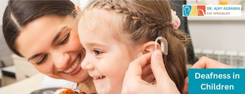 A smiling woman helps a young girl with a hearing aid. The girl has braided hair and looks happy. The text "Deafness in Children" is displayed on the image.